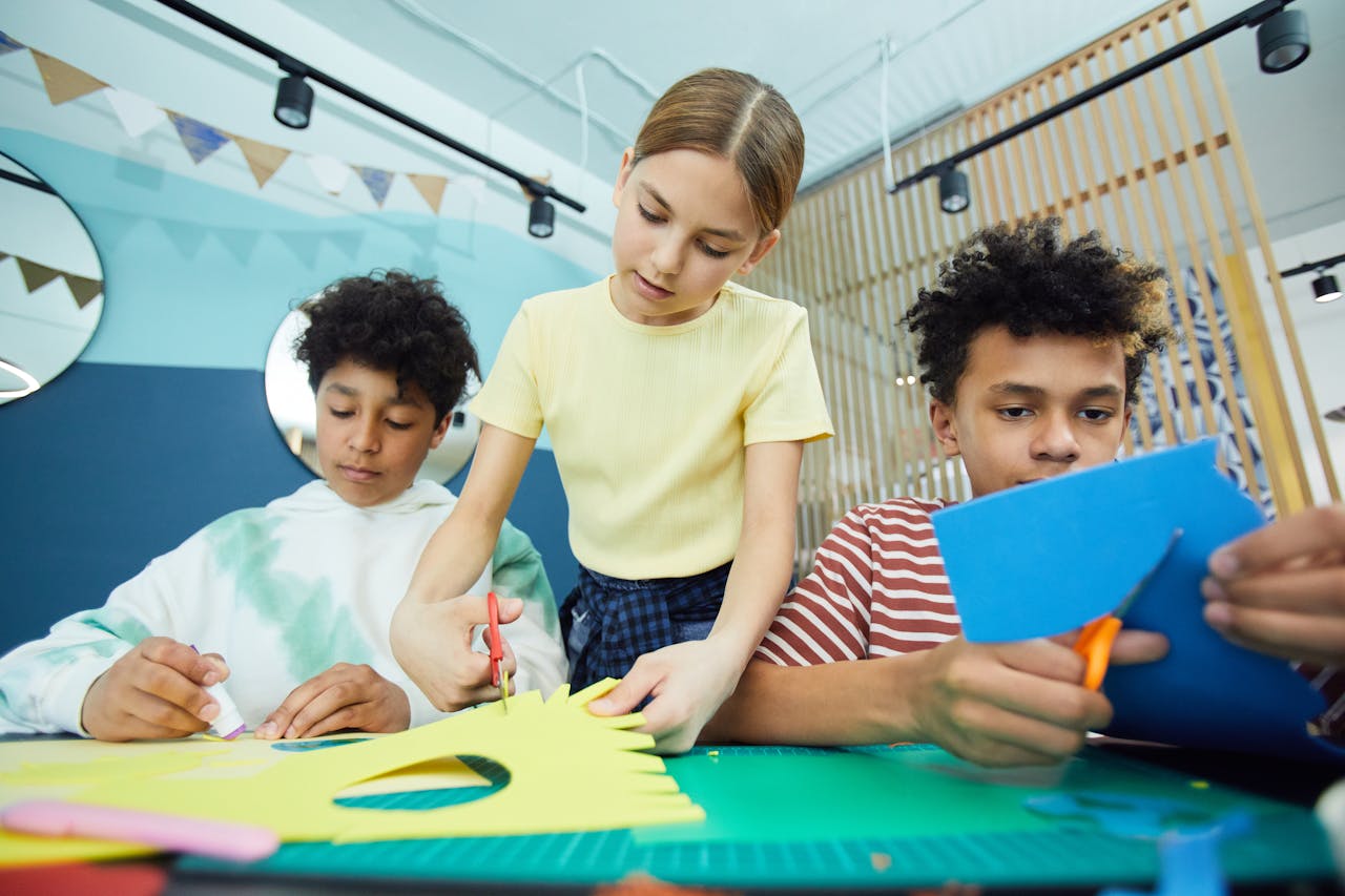 Three children engaged in a creative crafting session indoors, using paper and scissors.